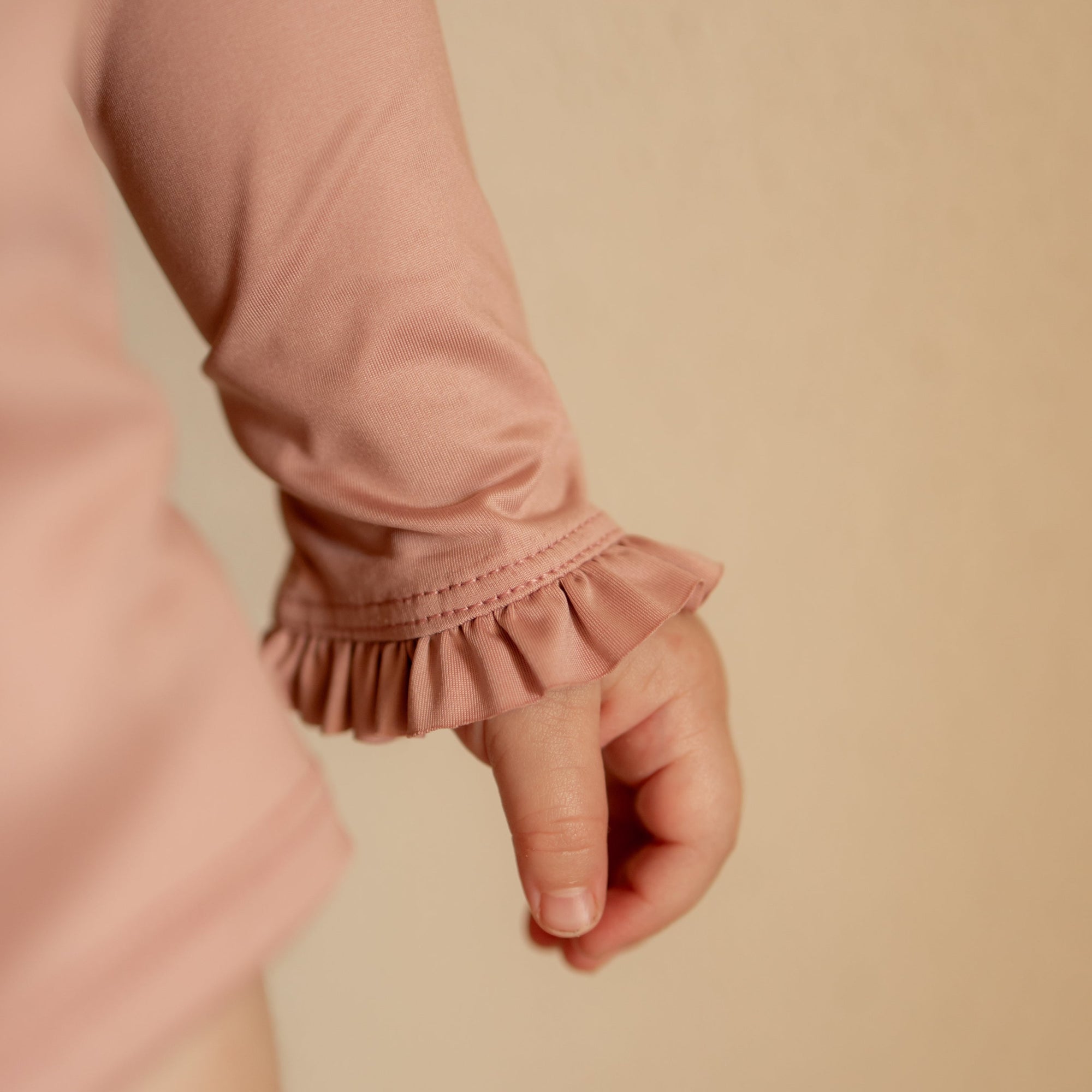 Close-up of a pink long-sleeve garment with ruffled cuffs on a beige background