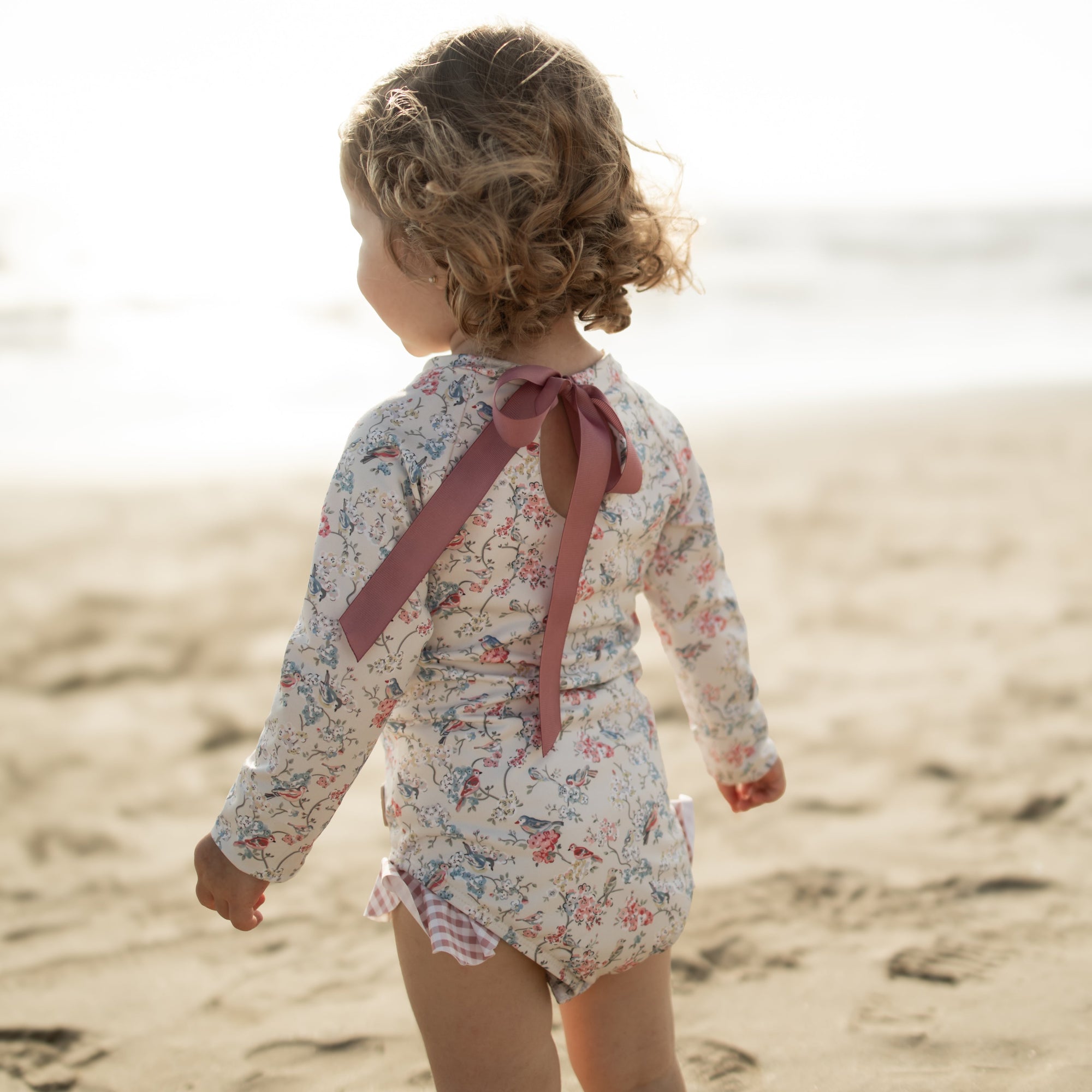 Child in a floral swimsuit with a bow on a beach
