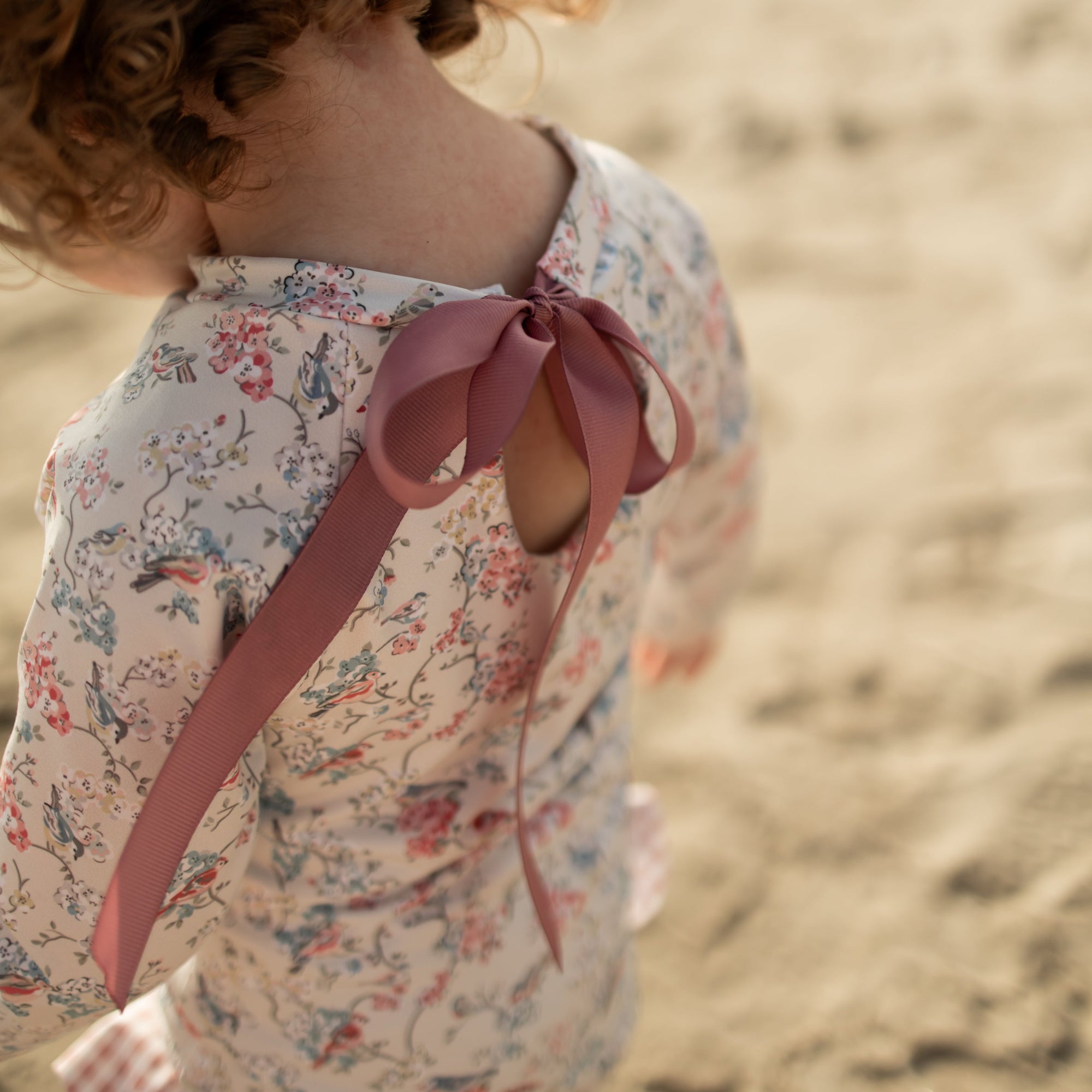 Child wearing a floral dress with a pink ribbon on a sandy background