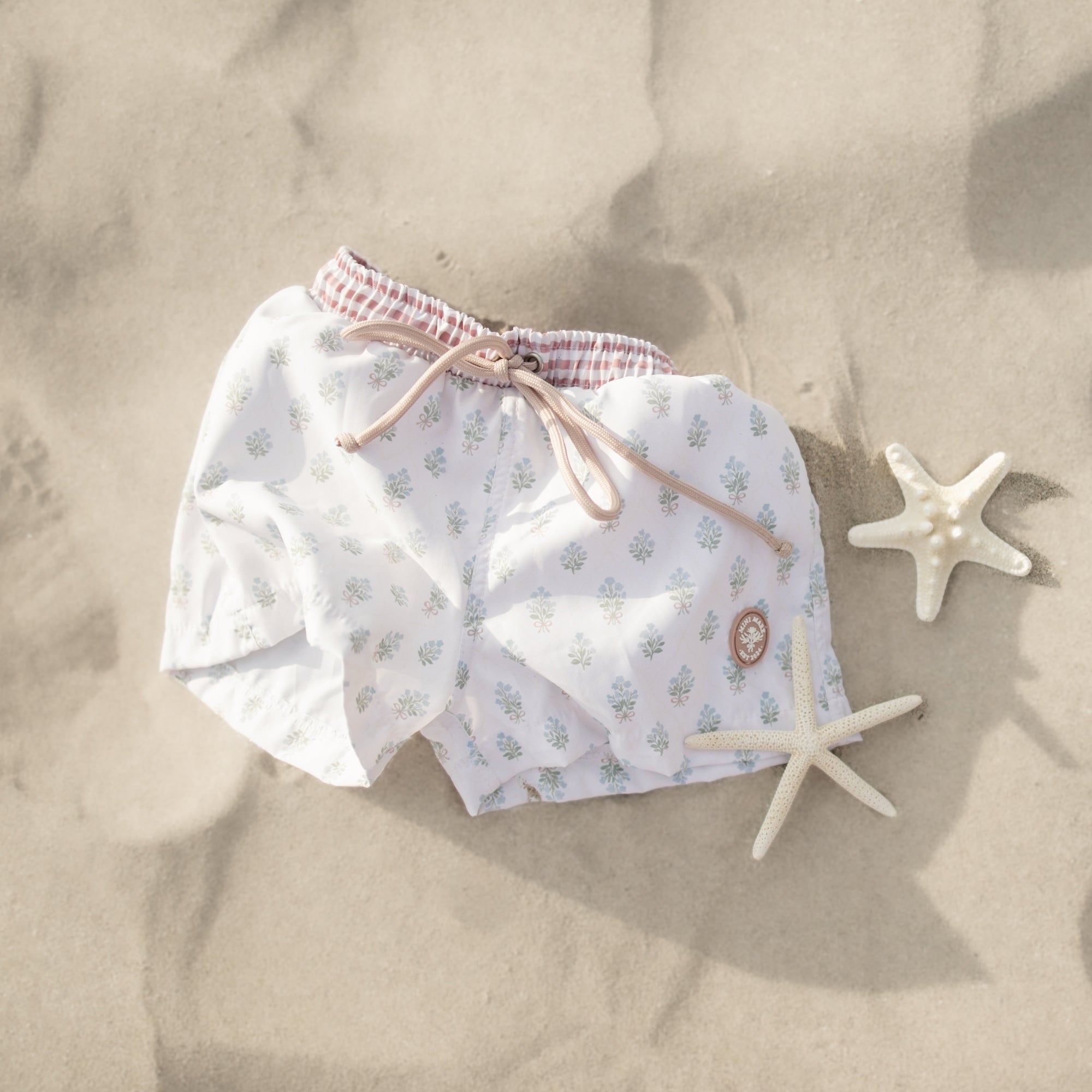 Floral-patterned shorts on sand with starfish