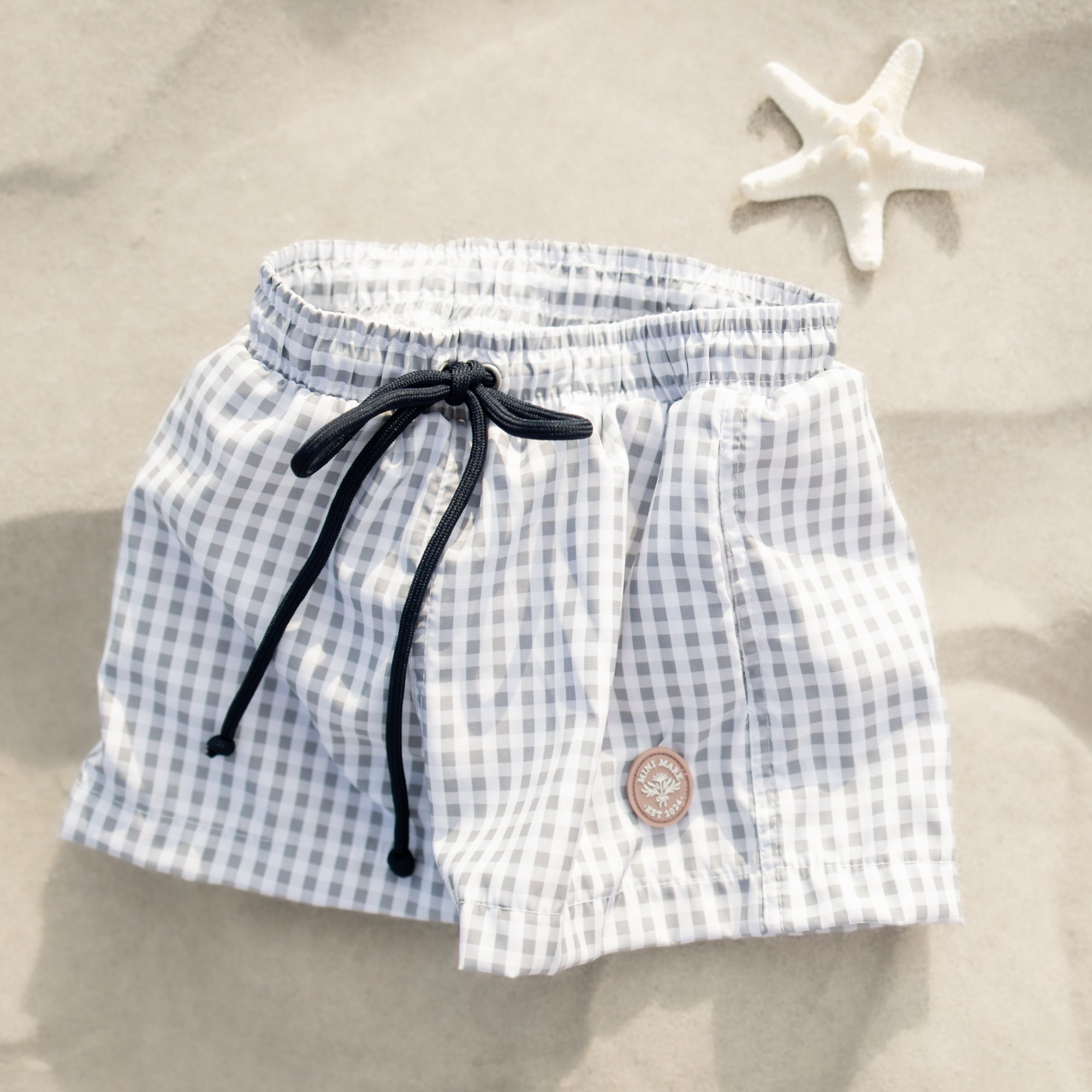 Blue and white checkered shorts with a black drawstring on a sandy background with a starfish.