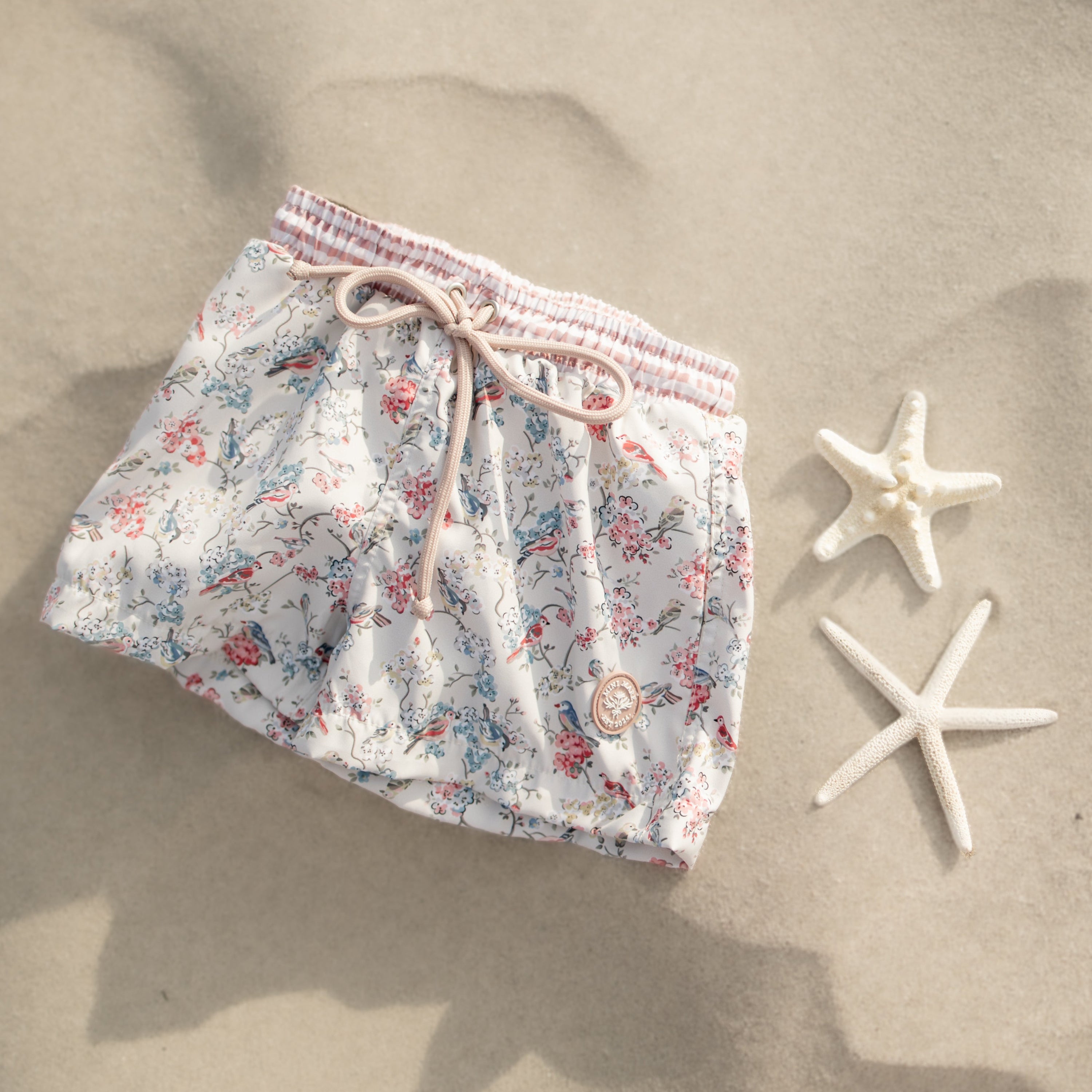 Floral swim shorts on sand with starfish