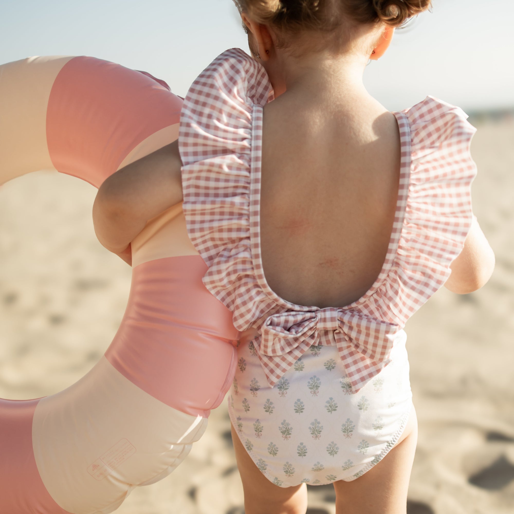Child in a checkered swimsuit with a pink and white inflatable ring on a beach