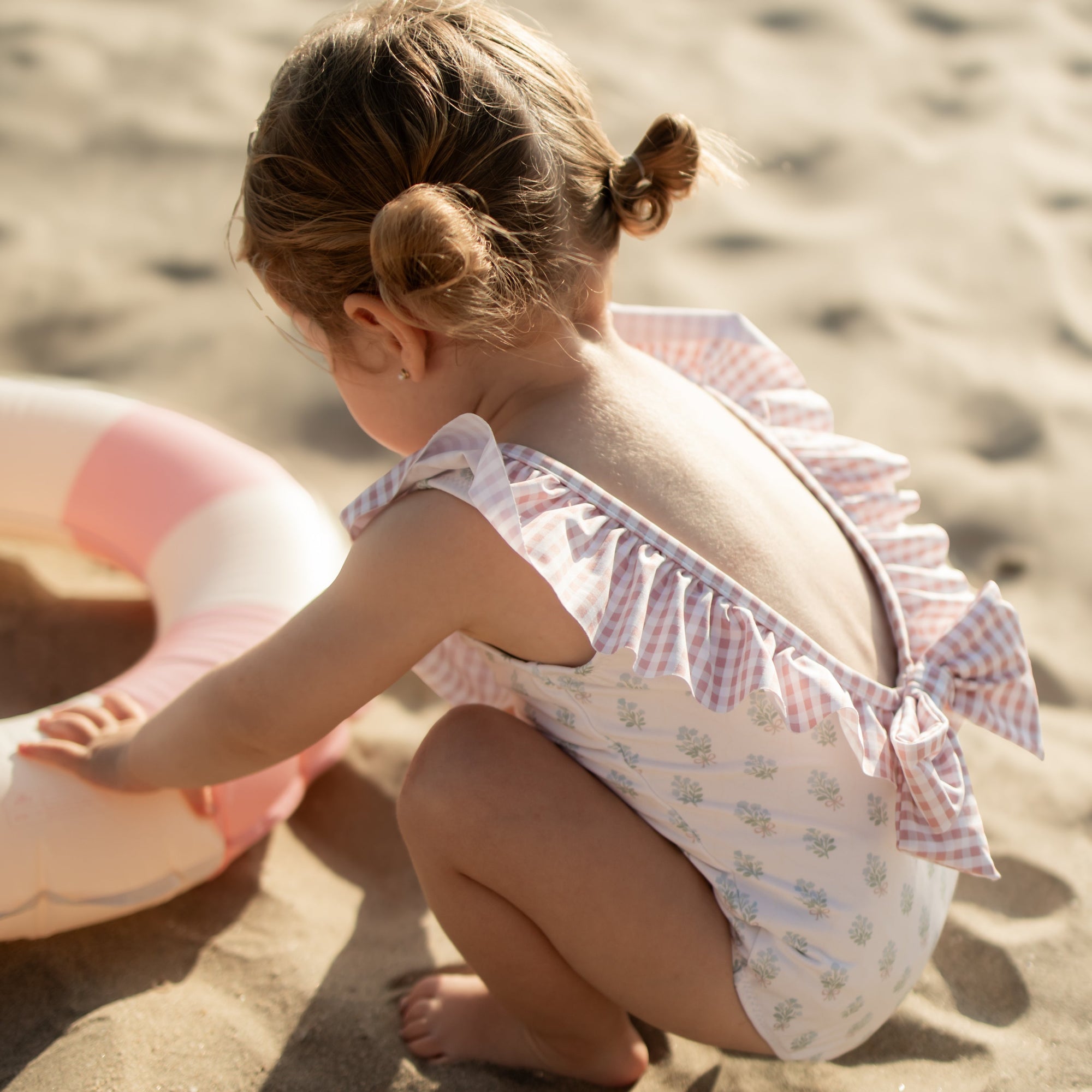 Child sitting on sand with a pink inflatable ring