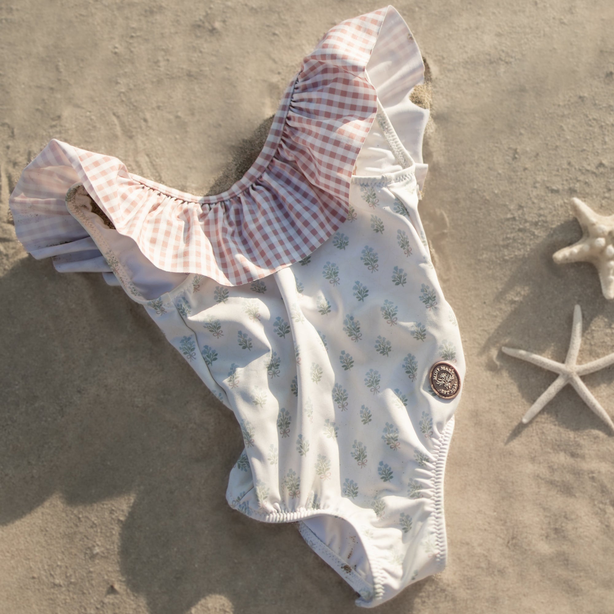 Baby outfit with ruffled top and patterned bottom on sand with starfish