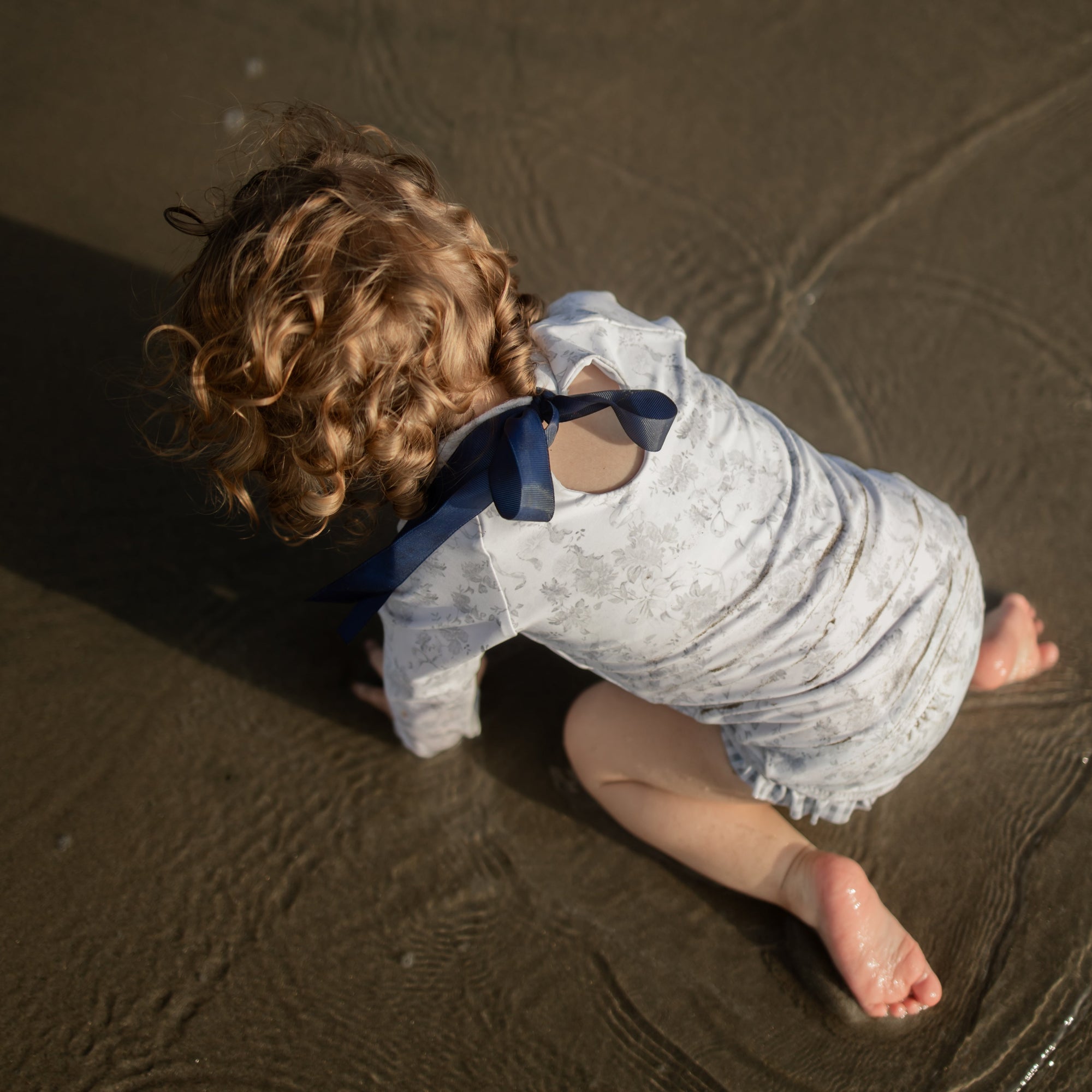 Child playing in sand with a blue bow tie