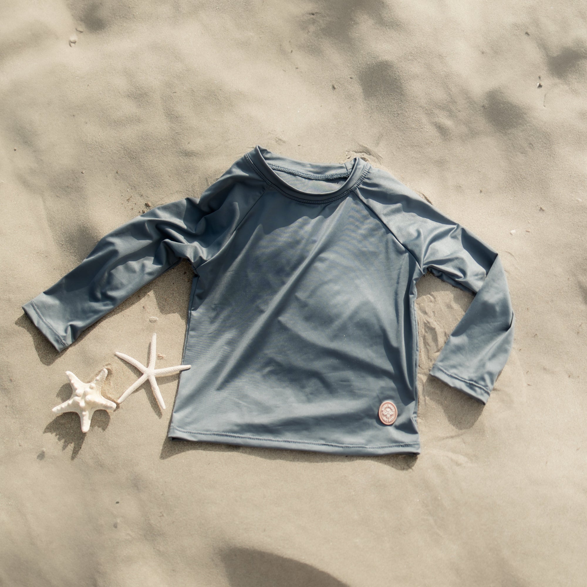 Blue long-sleeve shirt on sand with starfish