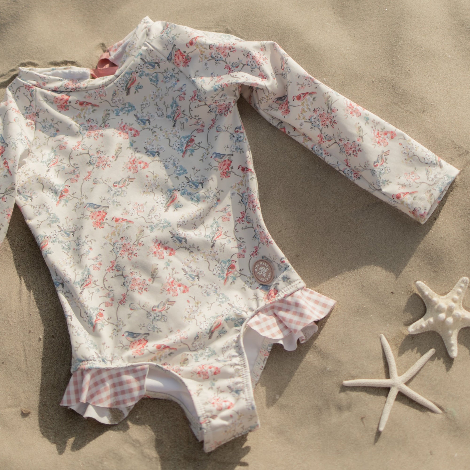Floral-patterned baby romper on sand with starfish