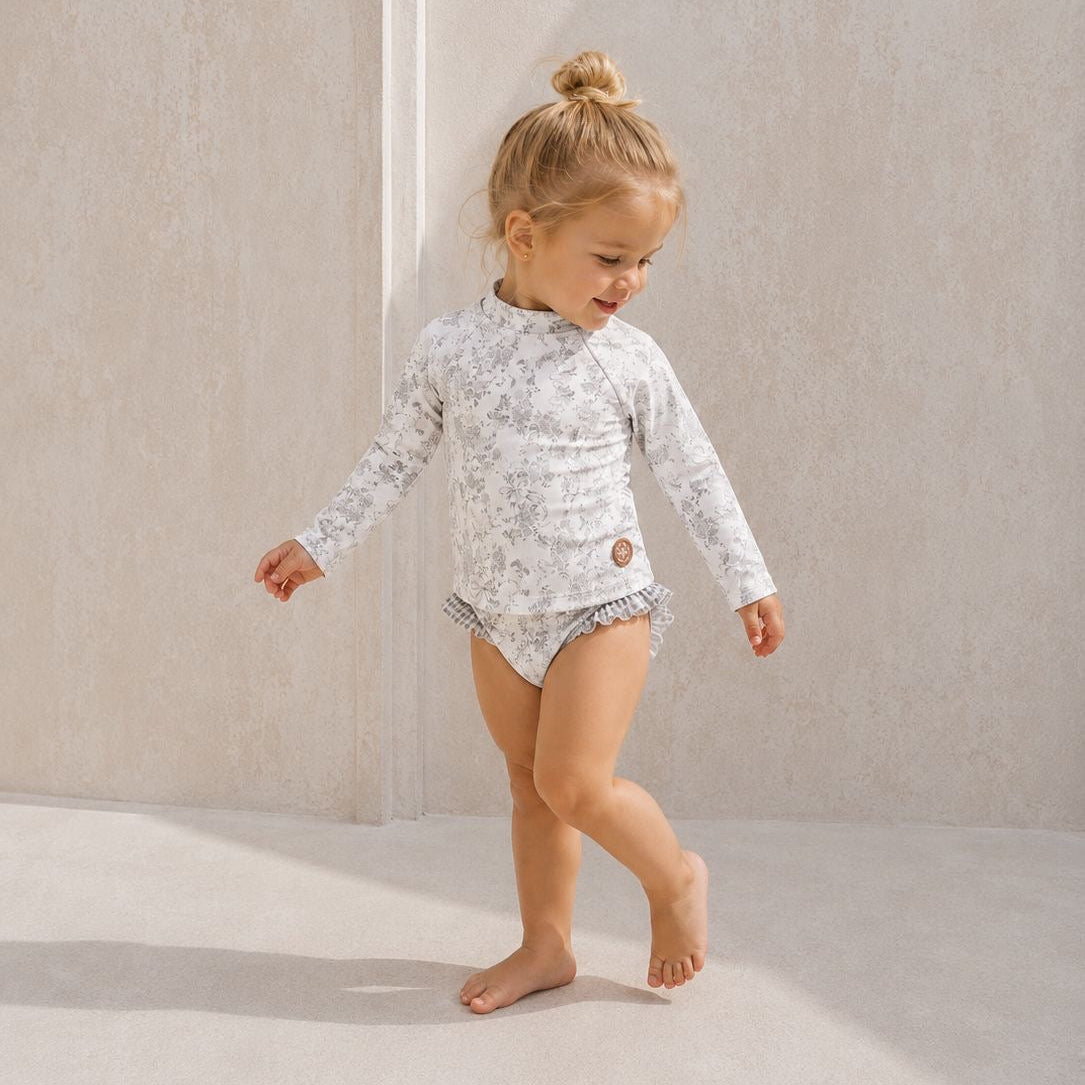 Child wearing a floral rash guard and diaper against a neutral background