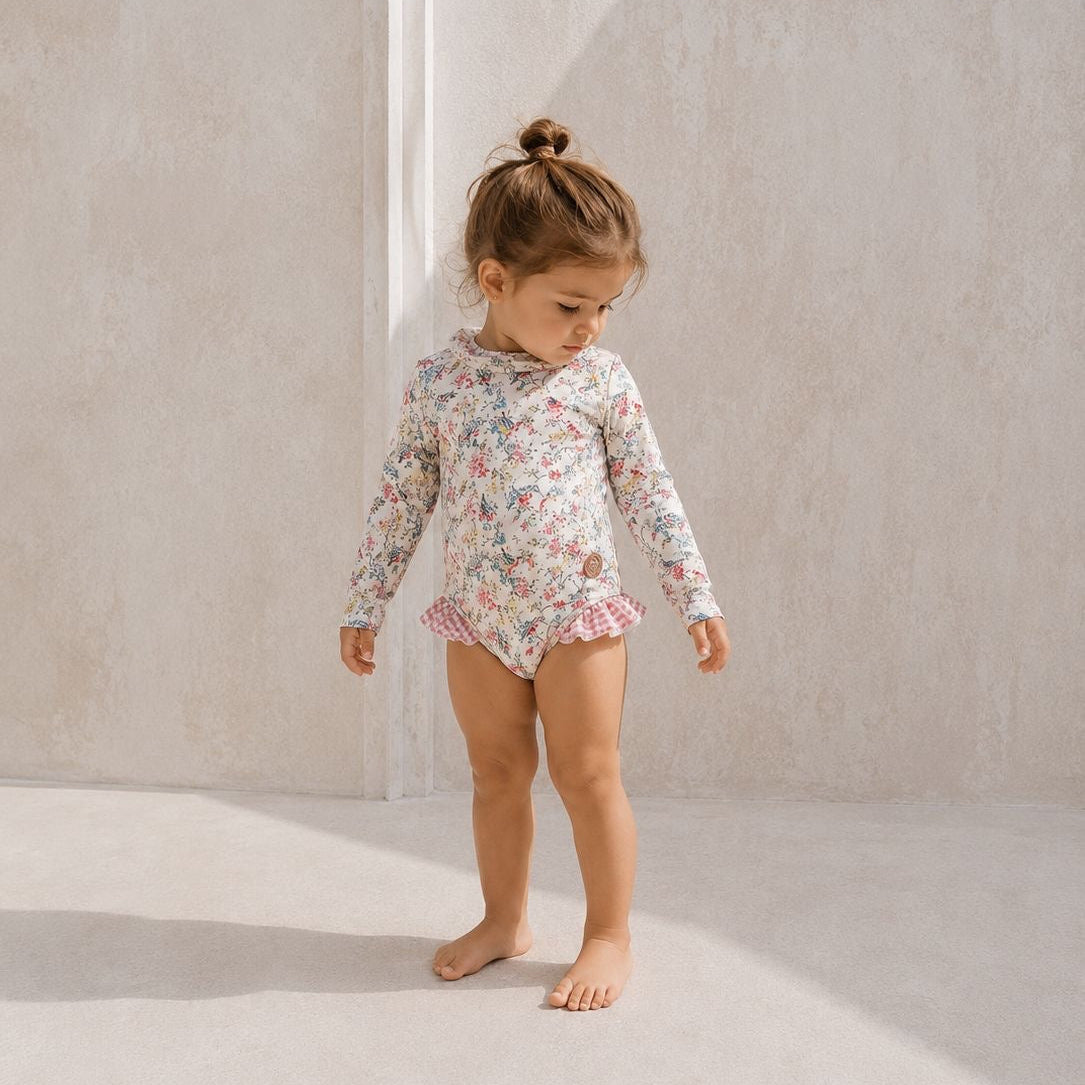 Young child wearing a floral swimsuit standing against a neutral background